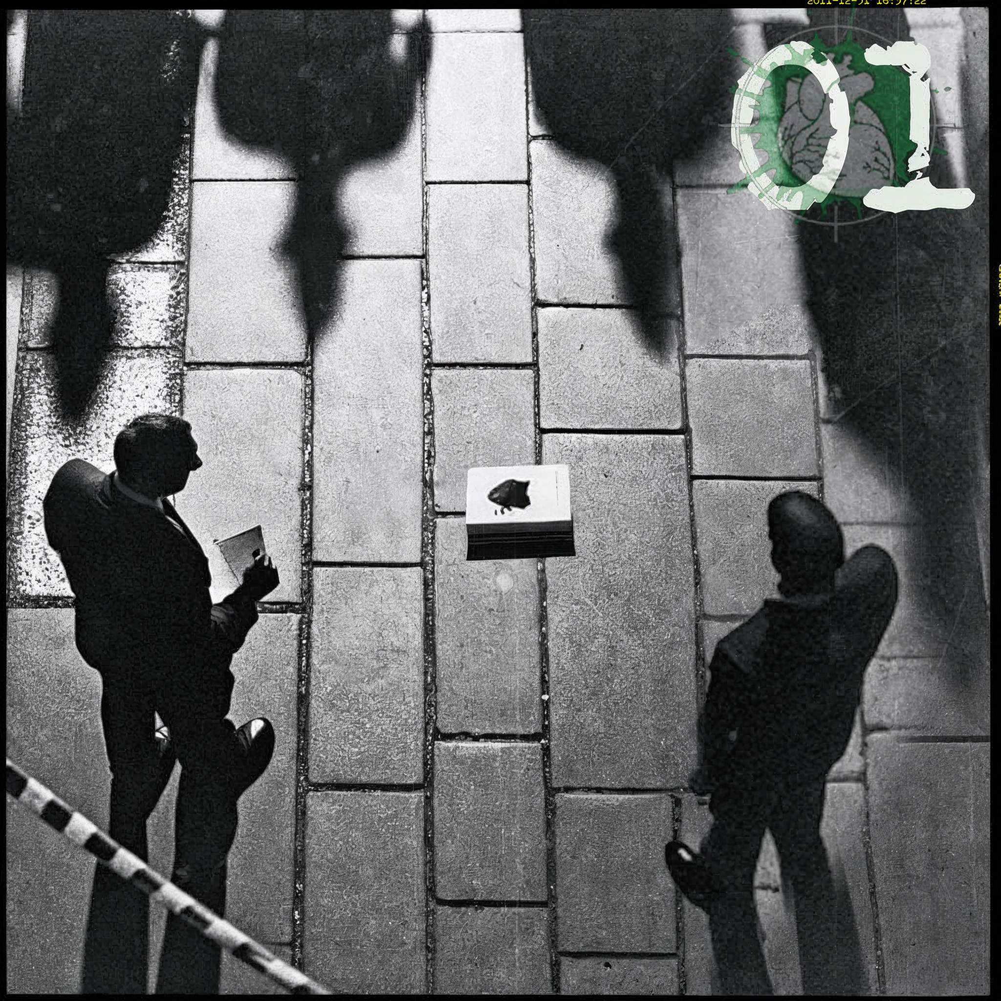 The cover art features a stark black-and-white photograph with a visible cut border. Viewed from above. It shows two men from above, behind a barrier tape on a paved floor with a stack of paper in the center and long shadows falling into the image. An overlay displays the number 01 over the pictogram of a human heart in the crosshairs. 